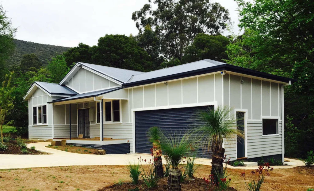 Grey weatherboard home with a painted garage and landscaped garden